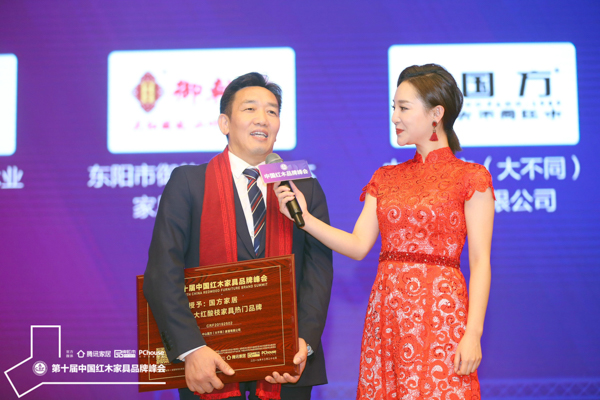 国方家居正接受湖北卫视主持人刘熙烨的台上采访，向大家介绍国方家居大红酸枝家具的特色